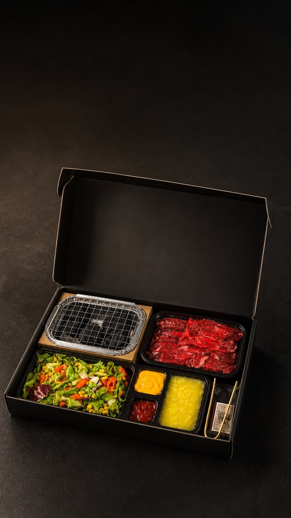 Eine offene Biteva-Box mit Tischgrill, mariniertem Fleisch, Salat, Saucen und Beilagen